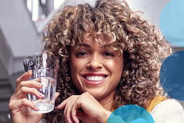 A woman smiling and holding a glass of filtered water.